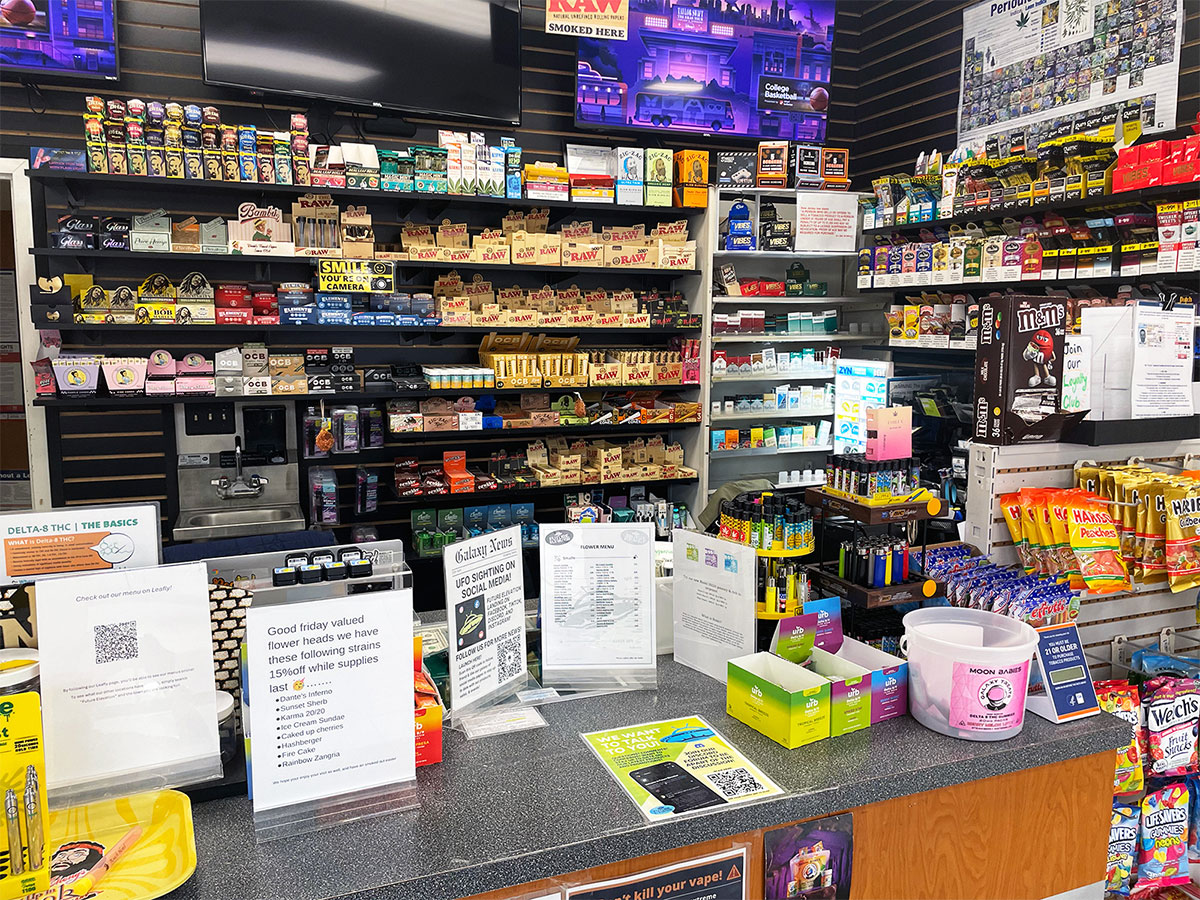 A sales counter with product display behind it with rolling papers, cigarettes, and other smoking accessory products at our Fanwood head shop and tobacco store.