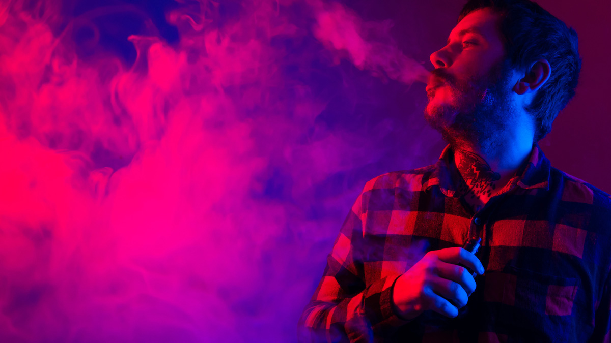 A man wearing a checkered shirt turning his head to the side and blowing out vapor from a THCa Vape near Austin, Texas.